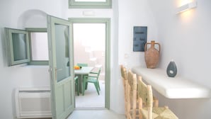 A room with a white wall, a green-framed window, a white air conditioner, a green table with chairs, and a shelf with decorative items. - Morfi Cave House (Santorini)