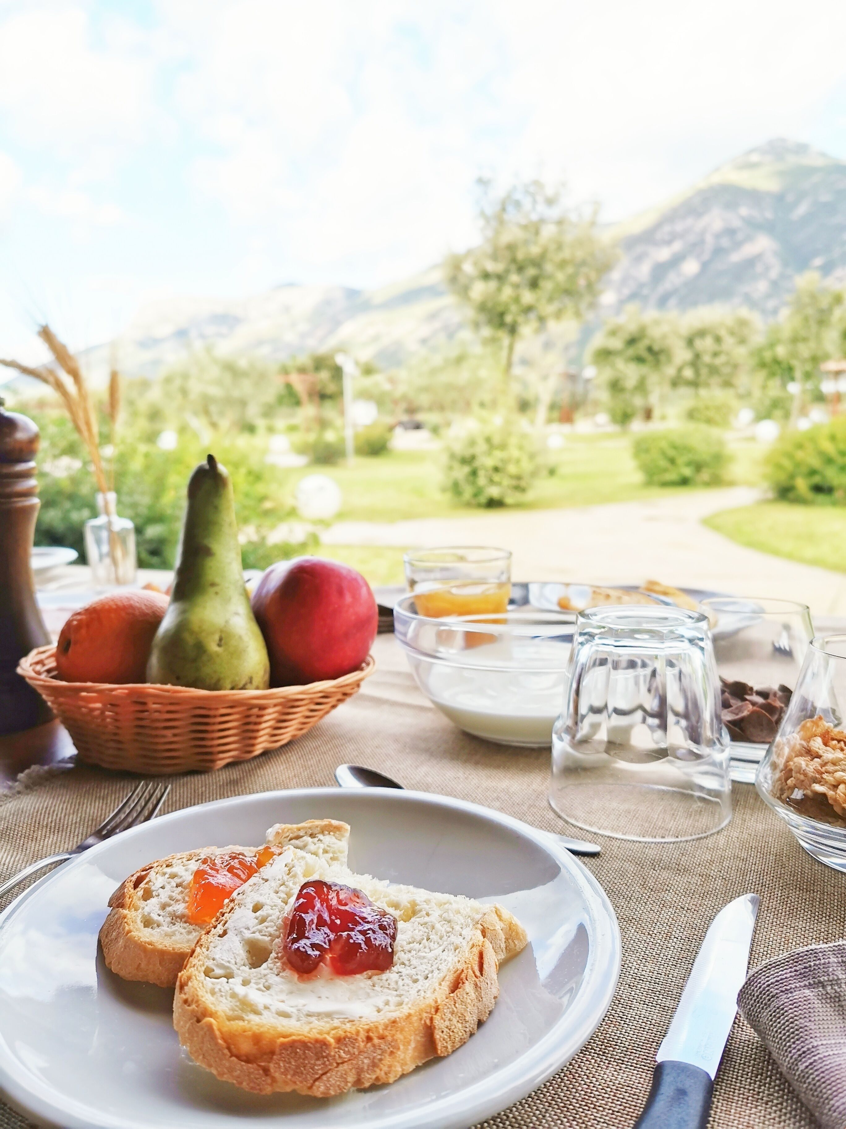 Un desayuno con tostadas, fruta y acompañamientos sobre una mesa, con una vista panorámica de montañas al fondo.