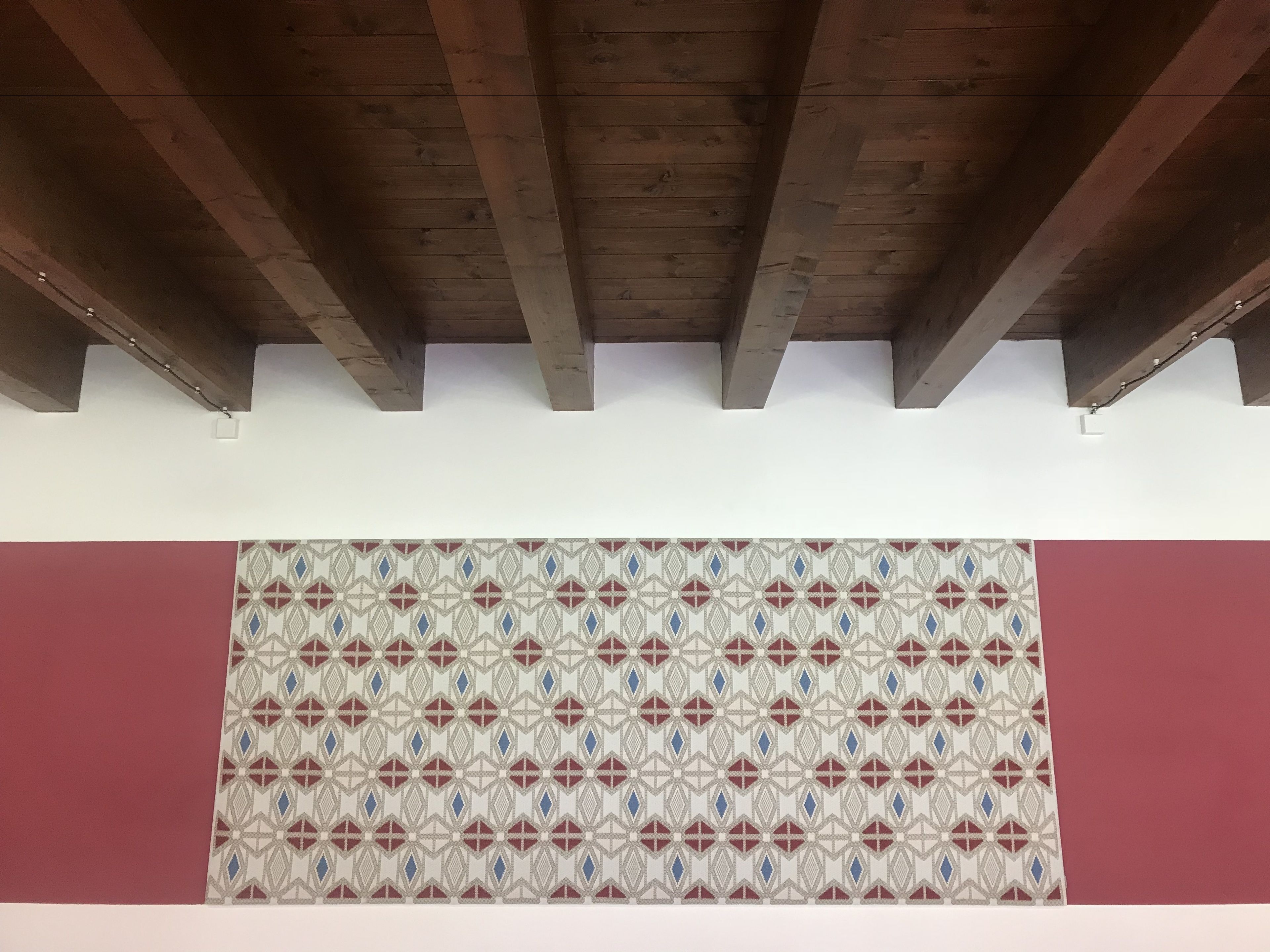 A room with a patterned floor, wooden ceiling beams, and a red wall.