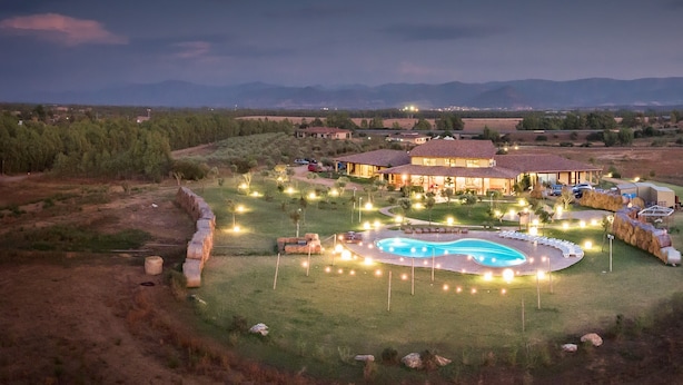 Un edificio amplio y bien iluminado con piscina central, rodeado de un jardín ajardinado y vistas a montañas lejanas.