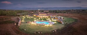 A large, well-lit building with a swimming pool in the center, surrounded by a landscaped garden and a view of distant mountains. - Agriturismo Saludi e Trigu (Iglesias)
