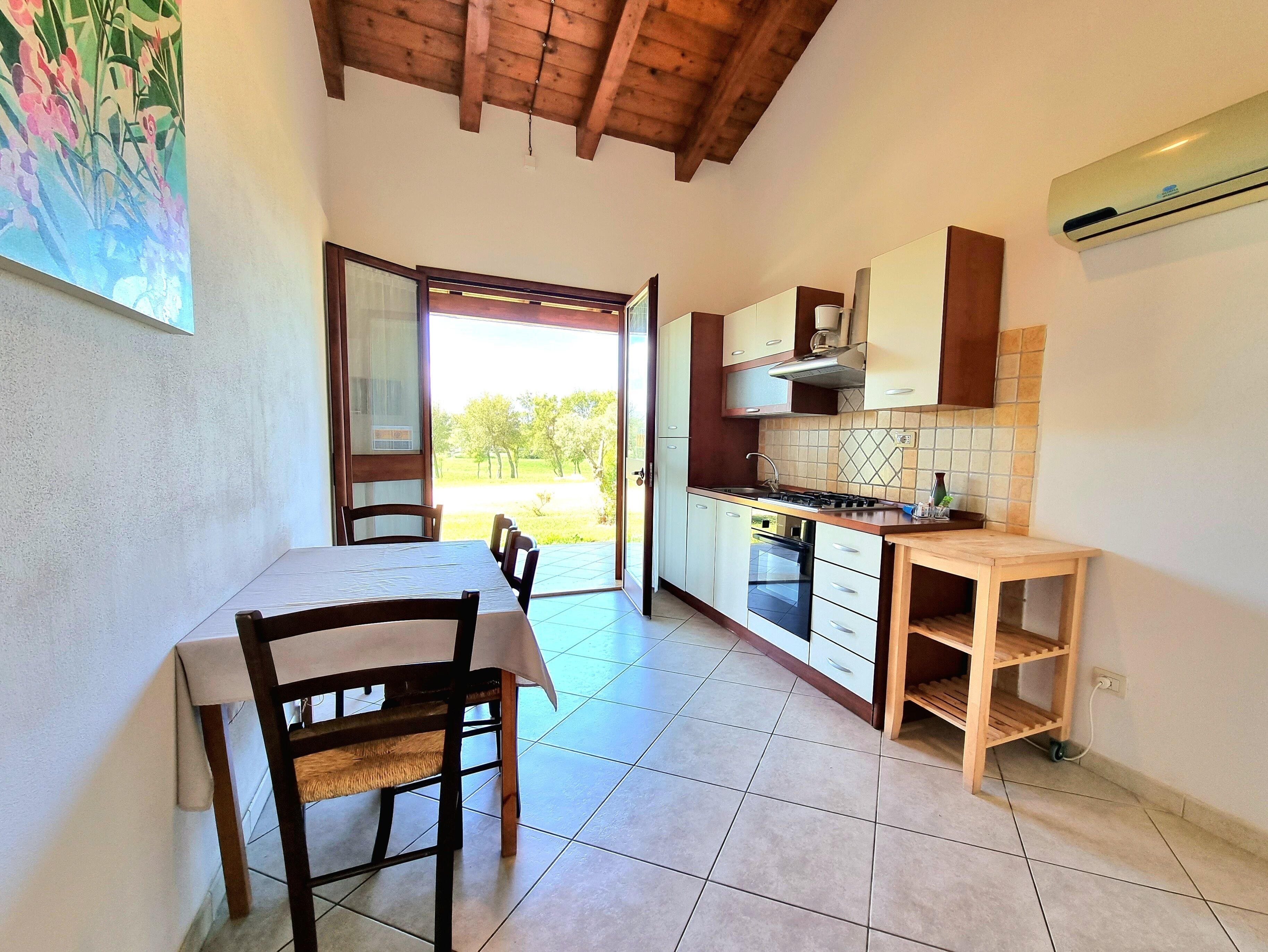 A kitchen with a dining area, wooden ceiling, tiled floor, and a view of the outdoors.