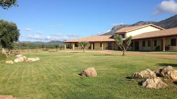 A two-story building with a tiled roof, a grassy lawn, and large rocks.