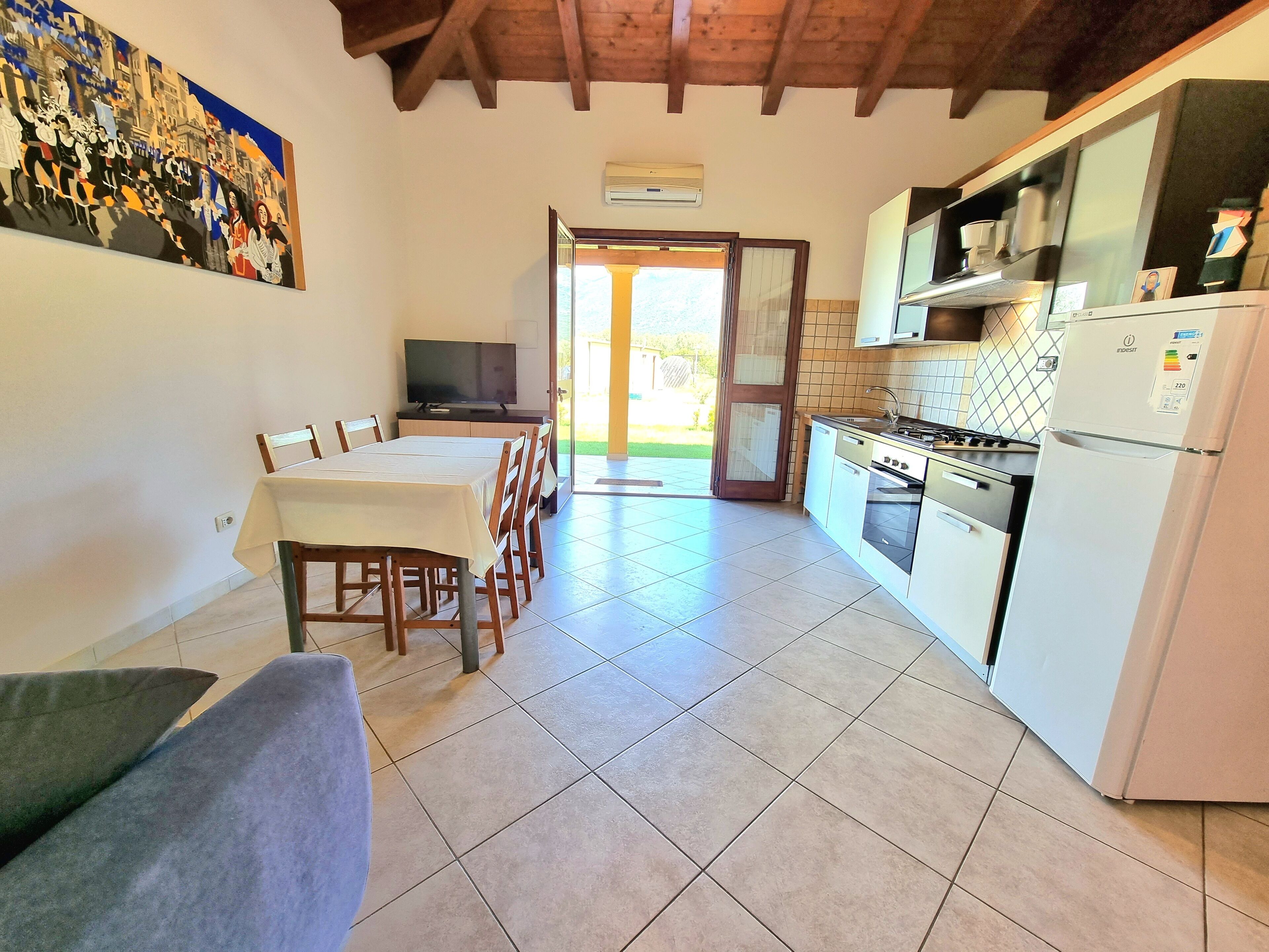 A dining area with a table and chairs, a kitchen with appliances, and a painting on the wall.