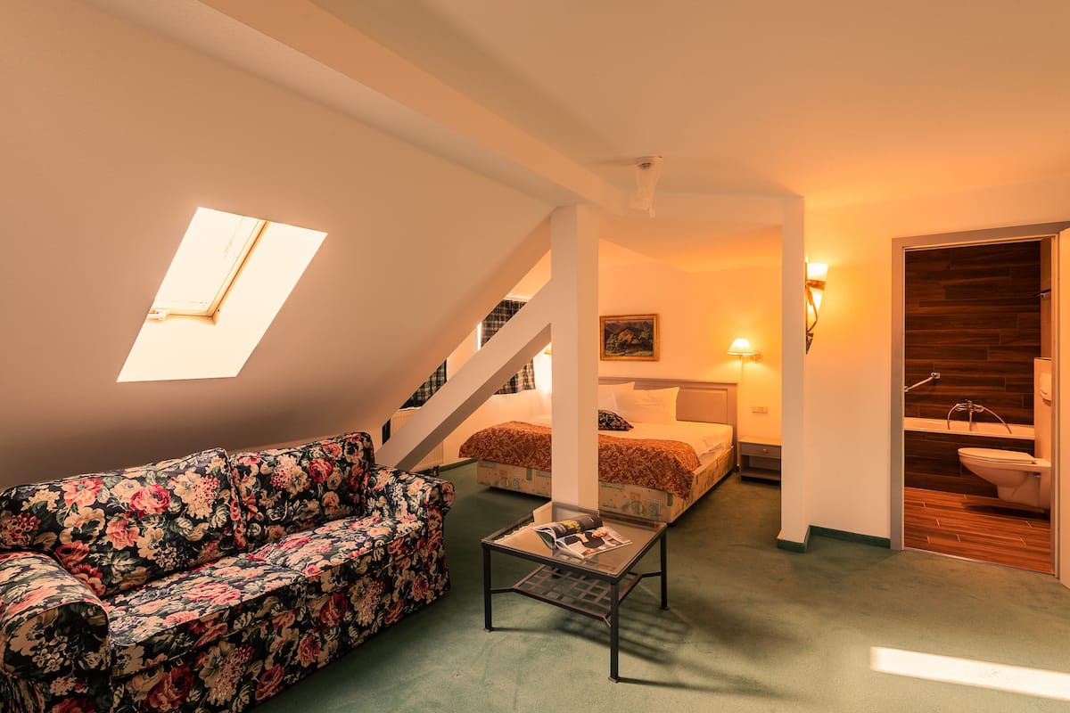 A room with a sofa, a small table, a bed, a staircase, and a bathroom.