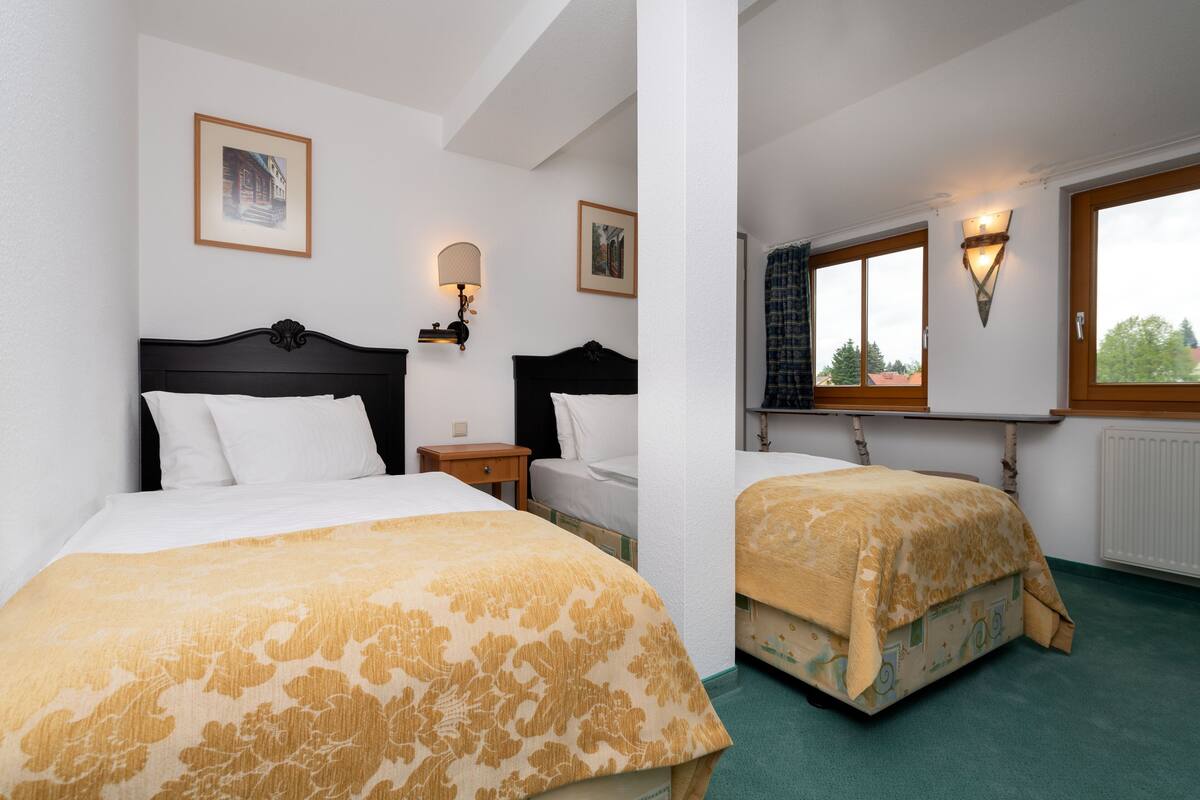 A hotel room with two beds, a nightstand, a lamp, and a window with curtains.