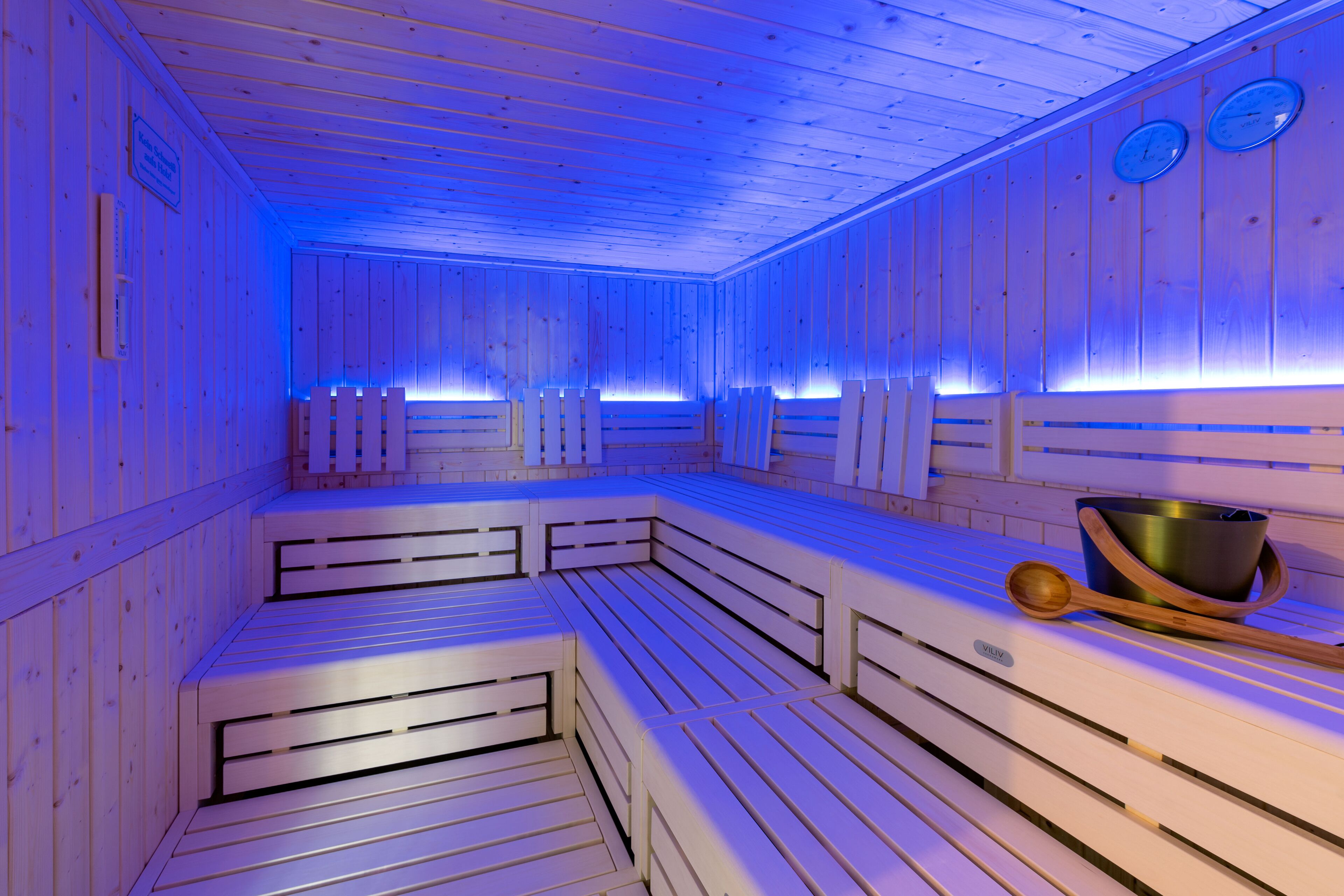 A sauna with wooden benches and benches, a wooden spoon, and a metal container on the bench.