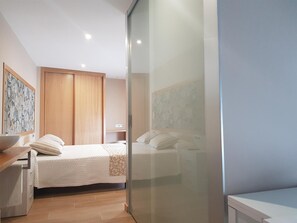 A bedroom with two beds, a wooden wardrobe, a bedside table, and a wall-mounted artwork. - Casa Chelo Alojamientos (Mazaricos)