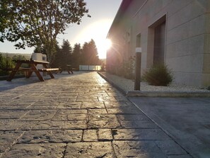 Un espacio al aire libre con pavimento, una mesa de picnic y un edificio con una persiana cerrada.