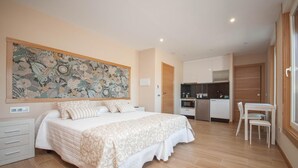 Un dormitorio con una cama grande, una mesa de comedor y una kitchenette al fondo.