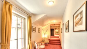 A spacious room with a red carpet, a window with yellow curtains, a floral chair, and a staircase leading to another area. - Hotel Drachenwand - Mondsee (Sankt Lorenz)
