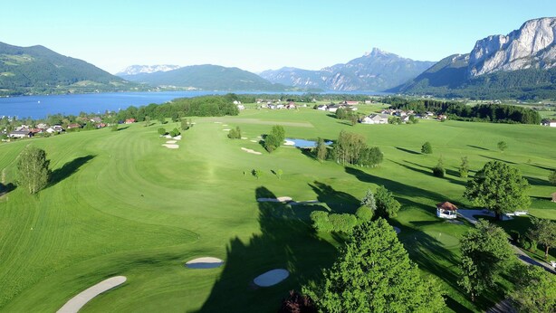 A golf course with bunkers, a pond, and houses in the background. - Hotel Drachenwand - Mondsee (Sankt Lorenz)