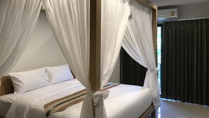 A four-poster bed with white linens and sheer drapes, a wooden headboard, and a dark curtain on the window.
