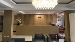 A hotel reception area with a wooden reception desk, a chandelier, and a seating area with sofas.