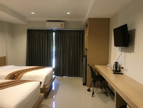 A hotel room with two beds, a desk, a chair, a television, and an air conditioning unit.