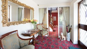 A room with a large ornate mirror, a wooden chair, a small table with a vase of flowers, and a patterned carpet. - Burswood Guest House (York)