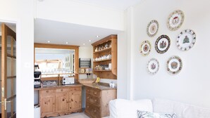 A kitchen with wooden cabinets, a coffee station, and a dining area with a white sofa and decorative plates on the wall. - Burswood Guest House (York)
