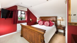 A bedroom with a wooden bed, red walls, a window with curtains, a bedside table with a lamp, and a large mirror. - Burswood Guest House (York)