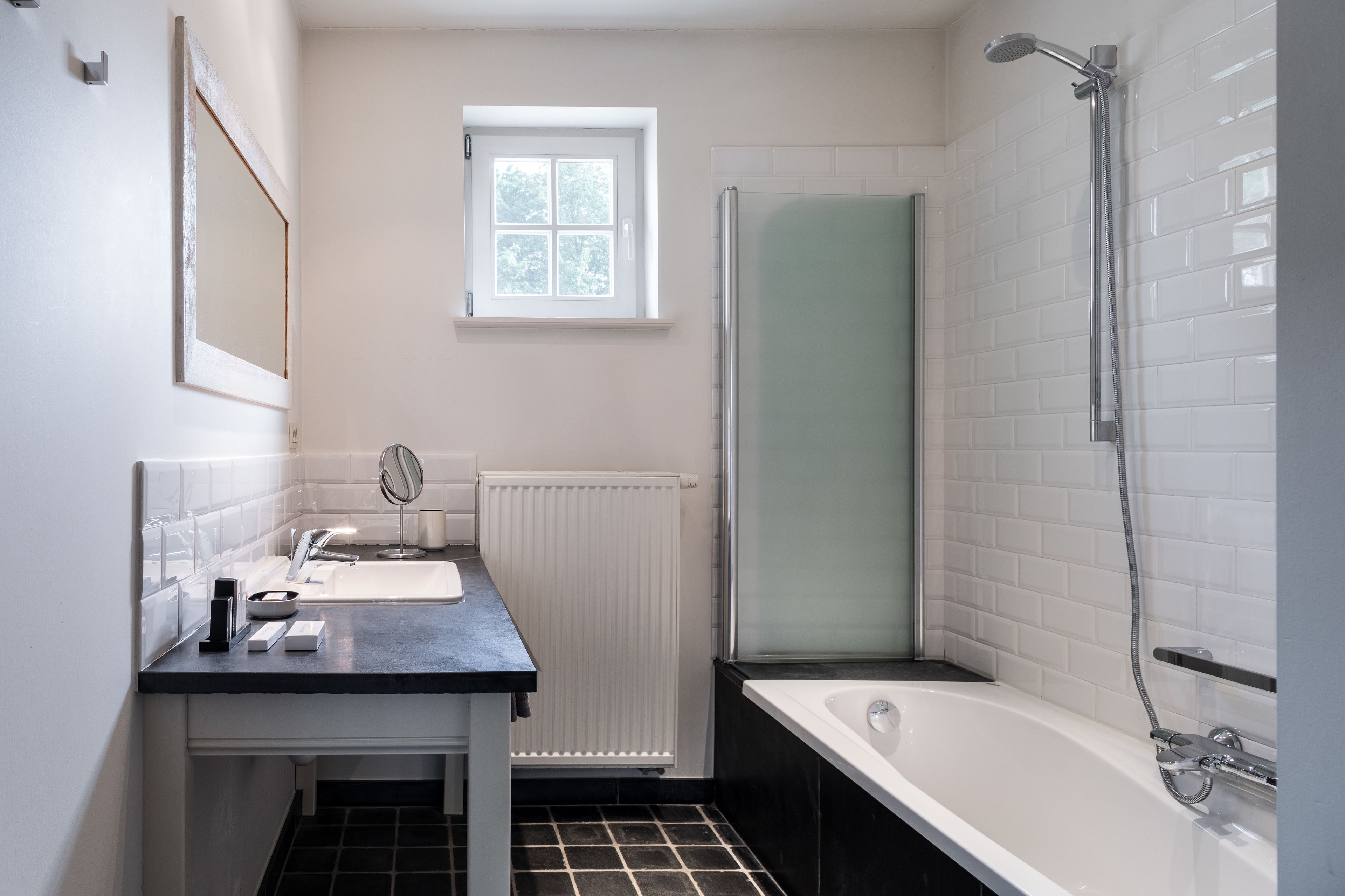 Une salle de bain avec un lavabo blanc, un miroir, une douche et une fenêtre.
