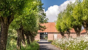 A pathway leading to a building with a brick facade and a red roof, surrounded by lush greenery and white flowers. - Holiday Home Babillie (Roeselare)