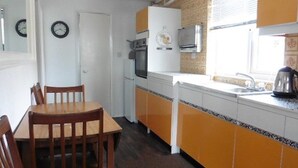 Une cuisine compacte comprenant une table et des chaises, un réfrigérateur, un four et une bouilloire posée sur le plan de travail.