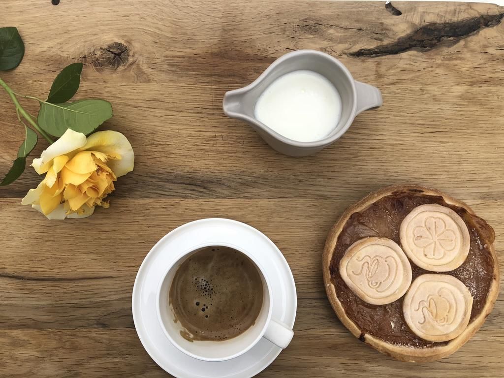 Una mesa de madera con una taza de café, un tazón pequeño de leche y un pastel con diseño de trébol.