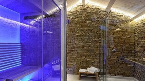 Un baño moderno con pared de piedra, cabina de ducha de vidrio y un banco con toallas.