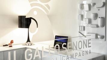 Quarto de hotel moderno com design minimalista, apresentando uma escrivaninha com um laptop, uma máquina de café embutida na parede e um luminário decorativo.