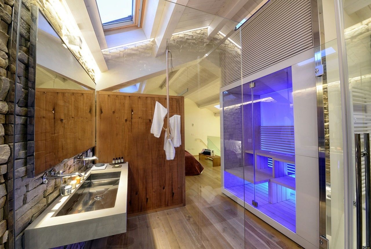 A modern bathroom with a stone wall, wooden paneling, a large mirror, a built-in sink, and a glass enclosure with blue lighting.
