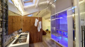 A modern bathroom with a stone wall, wooden paneling, a large mirror, a built-in sink, and a glass enclosure with blue lighting.