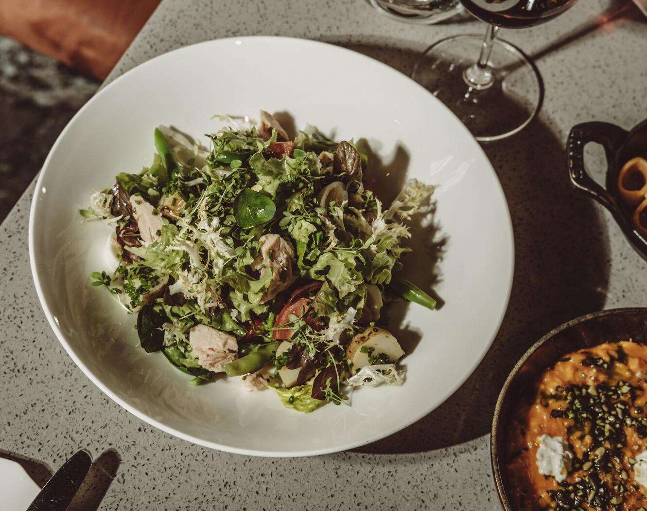 Een bord met gemengde salade, diverse groenten en mogelijk ook een beetje eiwit, geserveerd op een wit bord.