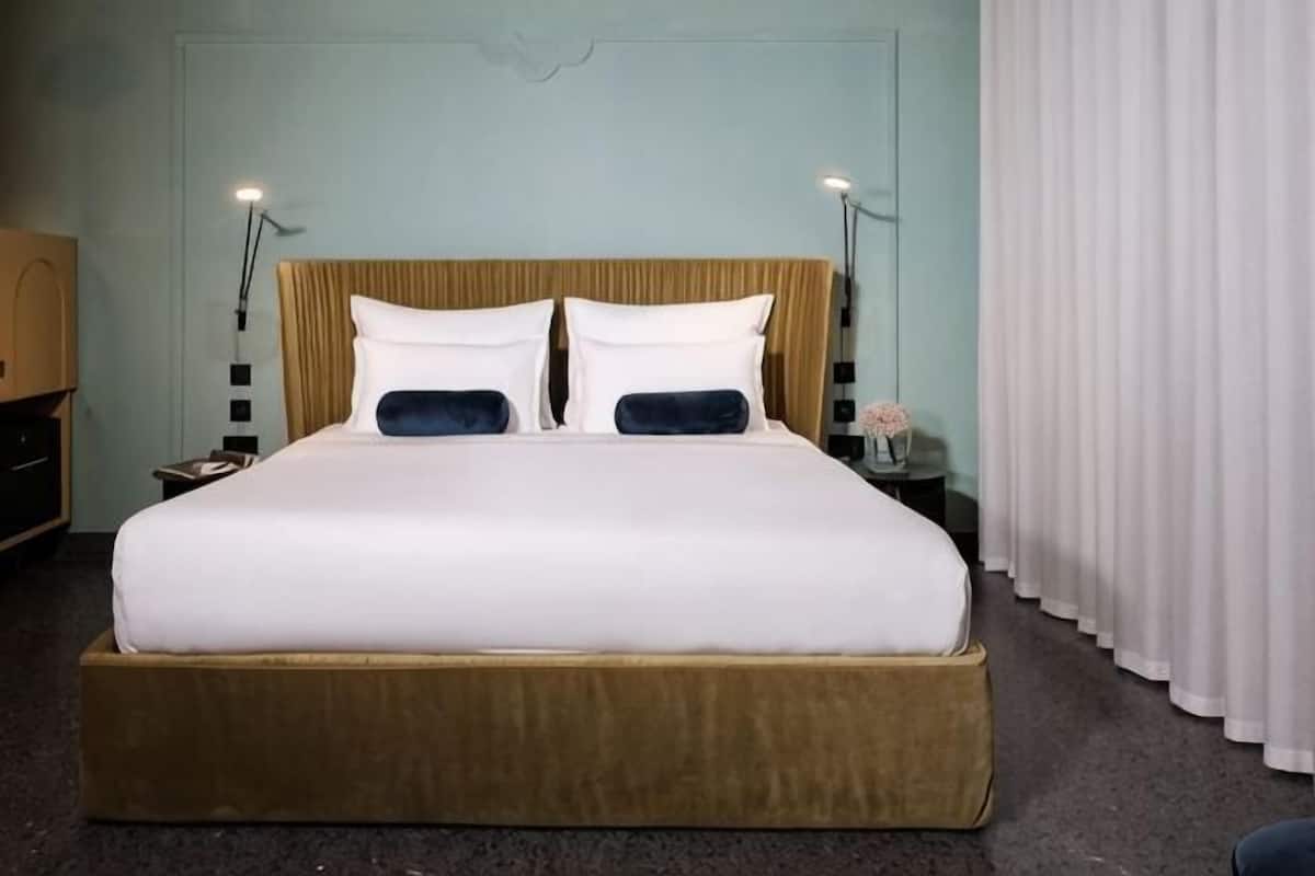 A hotel room with a large bed, two bedside tables, a nightstand, and a window with curtains.