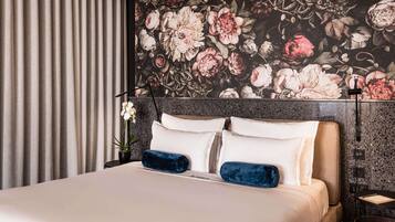 A hotel room with a bed, a floral wallpaper, a curtain, and a nightstand.