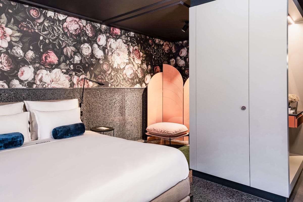 A modern hotel room with a large bed, a wardrobe, and a floral wallpaper design.