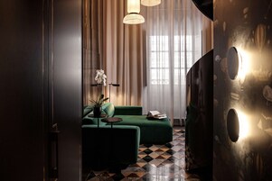 Una sala de estar moderna con un sofá verde, una mesita con una planta en maceta y un ventanal con cortinas translúcidas.