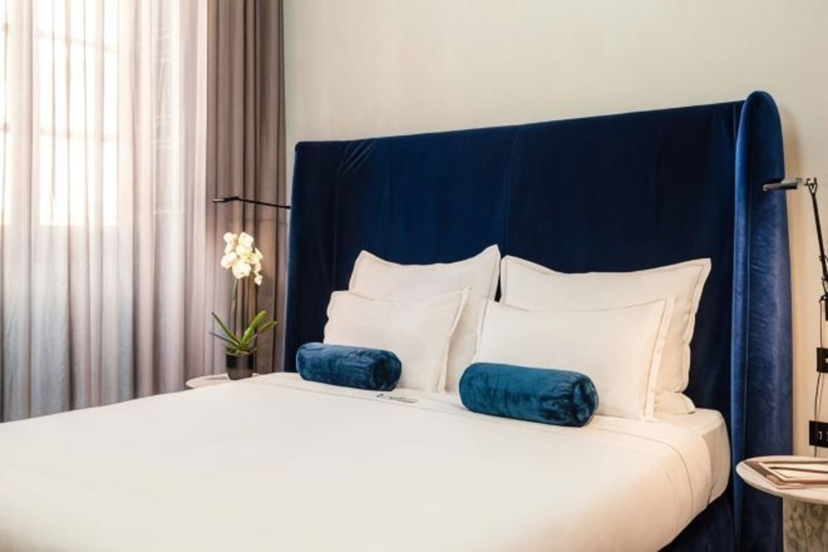 A bed with a dark headboard, white bedding, and two blue pillows.