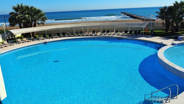 Una piscina grande y cristalina, con vistas al océano y a la playa.