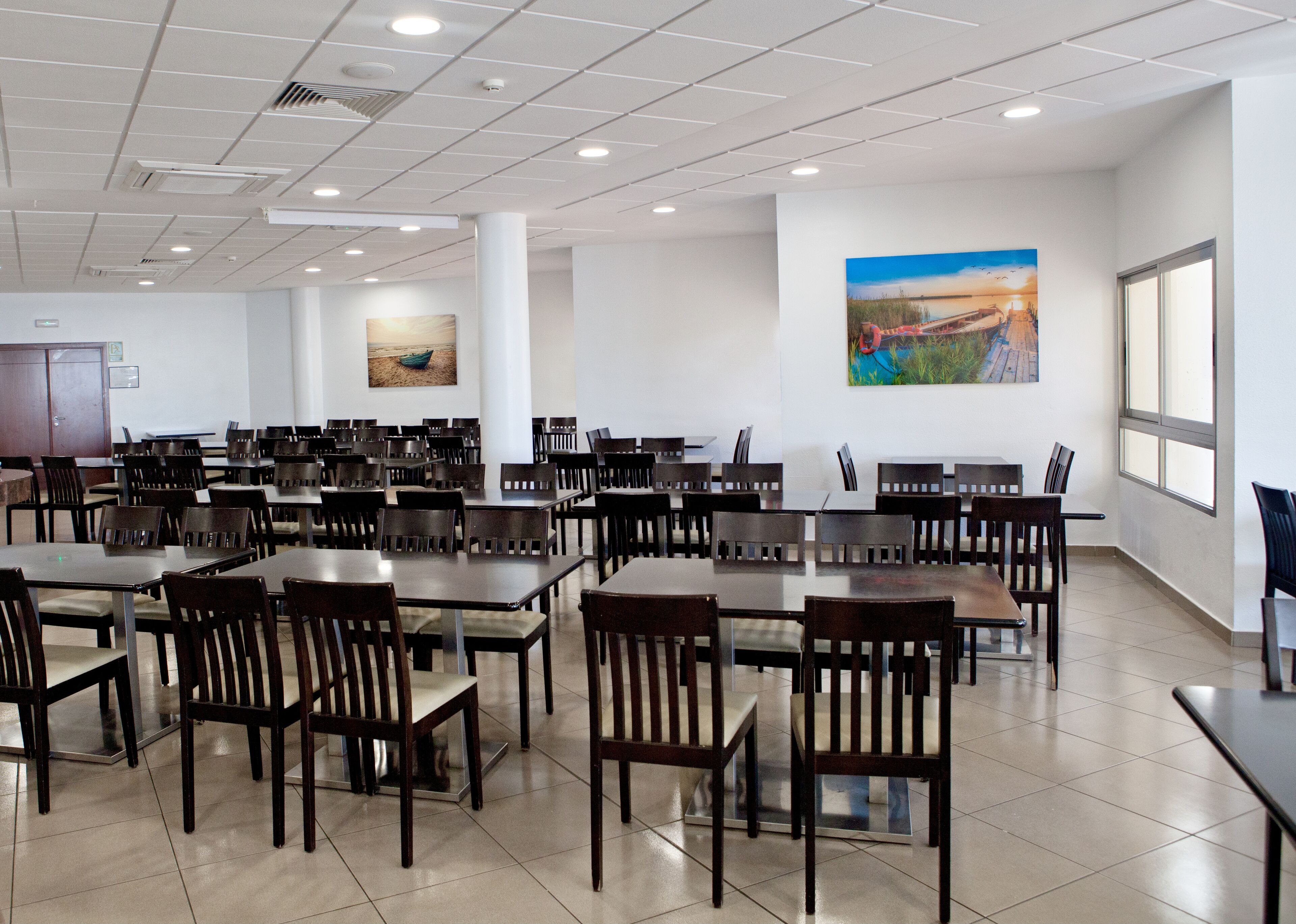 Un comedor amplio con varias mesas y sillas, ventanas grandes y obras de arte en las paredes.