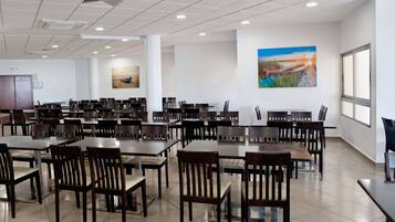 Un comedor amplio con varias mesas y sillas, ventanas grandes y obras de arte en las paredes.