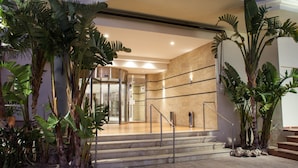 Una entrada de hotel moderna con una recepción de mármol, una escalera y plantas tropicales.