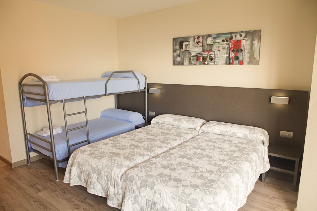 Um quarto com uma cama de solteiro, uma cama de casal e uma pequena mesa.