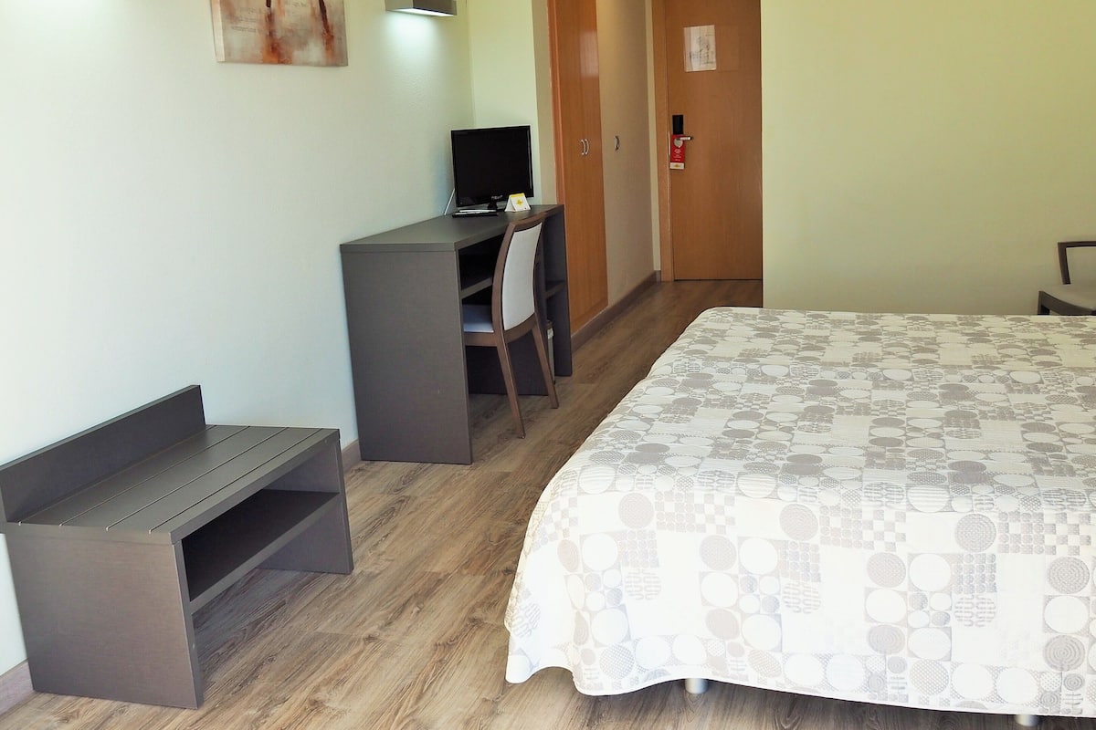 Quarto de hotel com cama, escrivaninha, cadeira e um pequeno espaço de estar.