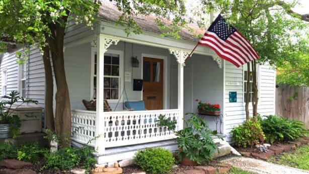 A white house with a porch, an American flag, and a mailbox.
