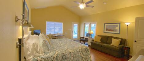 A bedroom with a bed, a desk, a chair, a sofa, and a ceiling fan.
