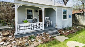 A small, single-story house with a porch, a swing chair, a rocking chair, and a small garden area with stepping stones and a bird bath.