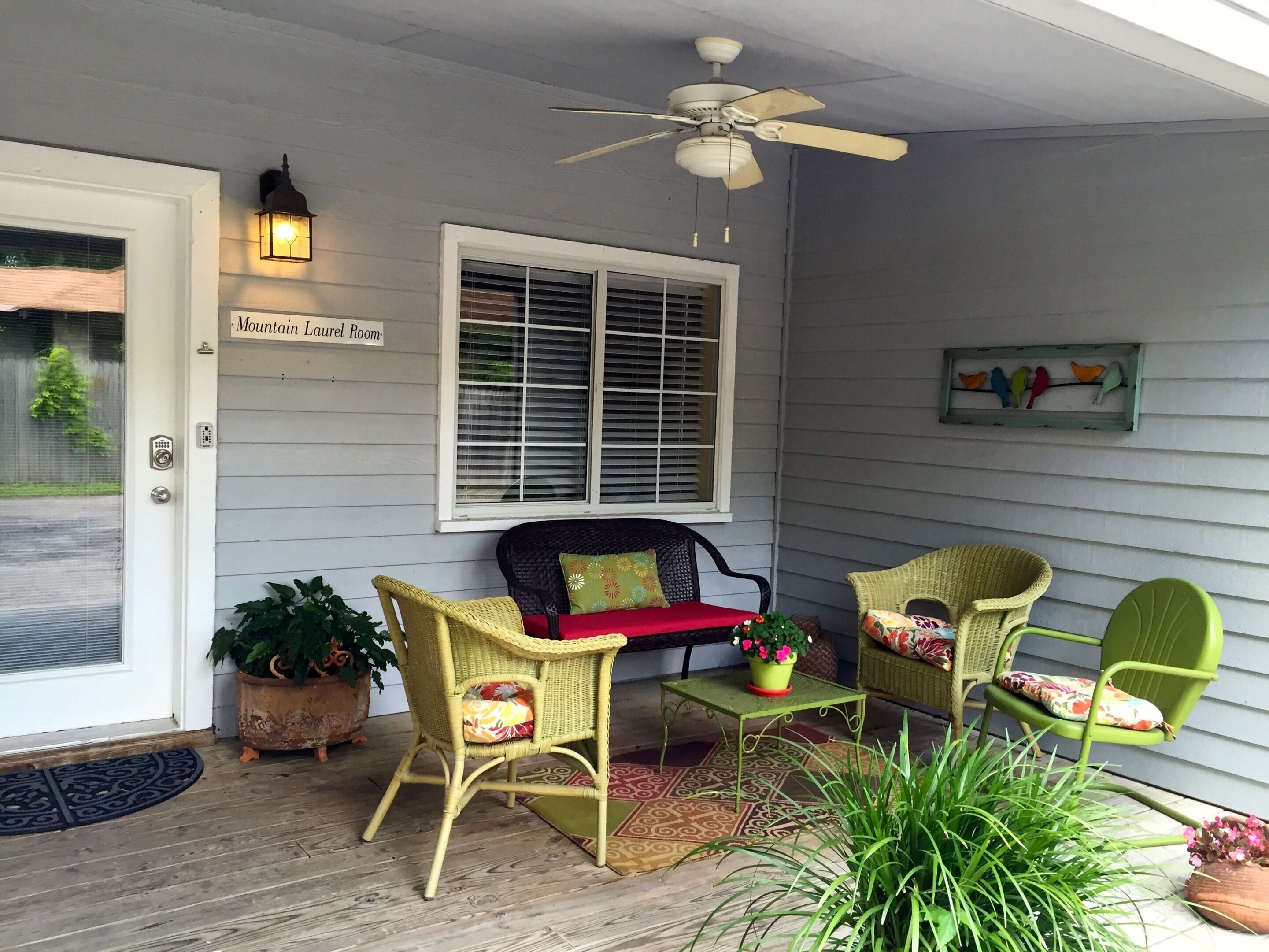 A porch with wicker furniture, a ceiling fan, a window with blinds, and a sign reading "Mountain Laurel Room".