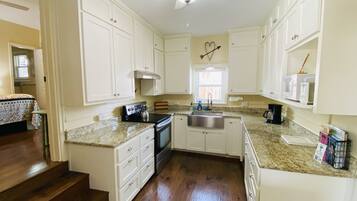 A kitchen with white cabinets, a stove, a sink, and a ceiling fan.
