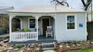 A small, single-story house with a porch, numbered 424, featuring a white picket fence, two chairs, and a small garden with rocks and plants.