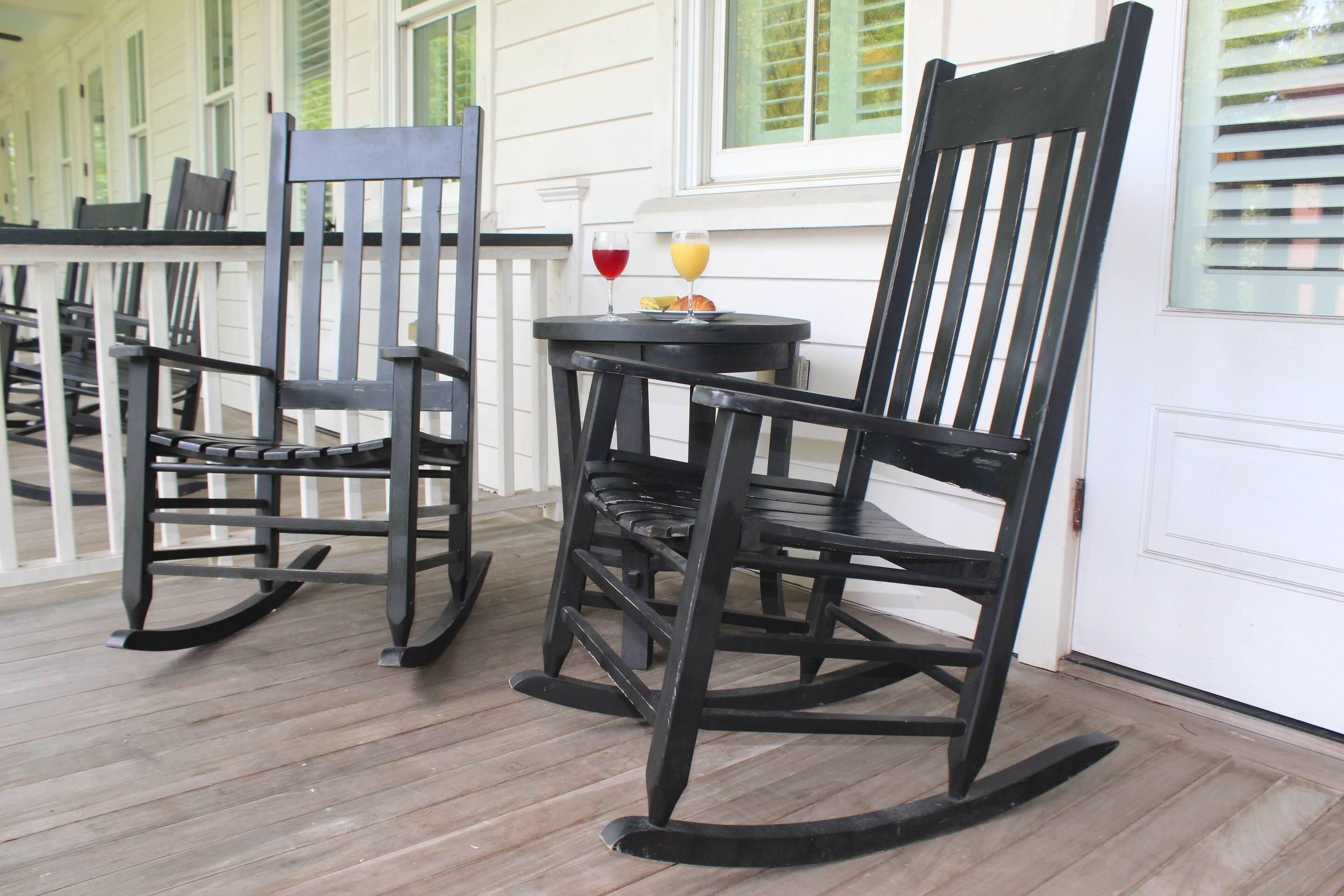 Two rocking chairs on a wooden deck with a table and chairs in the background.