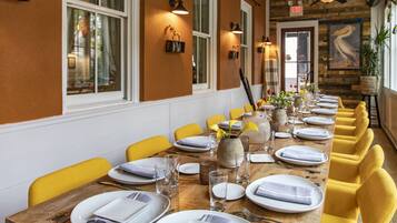 A long dining table with yellow chairs, white plates, and clear glasses set up in a room with wooden walls and windows.